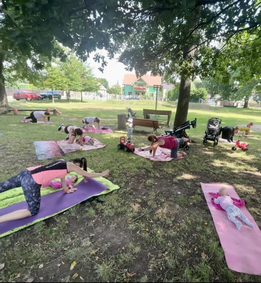 Maminky cvičí v parku, děti a kočárky hned vedle na dekách